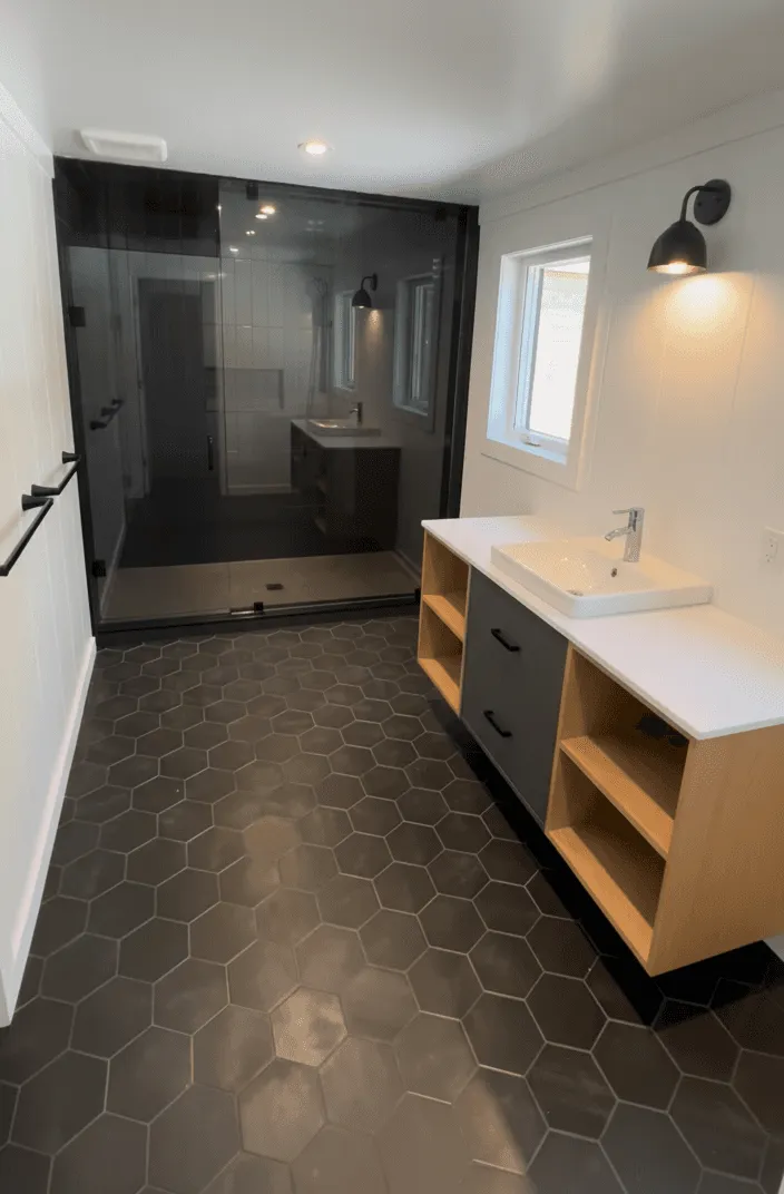 Finished bathroom with matte black hexagon floor tile, a black-framed glass walk-in shower and a floating oak vanity