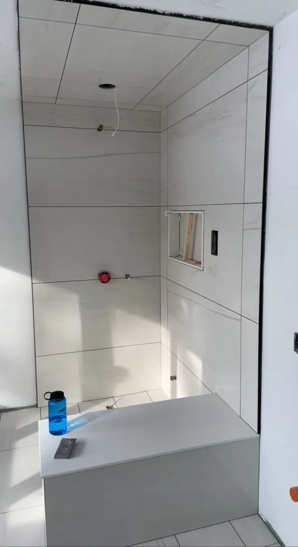 Shower in progress tiled floor to ceiling in large-format white porcelain with a built-in bench and a recessed niche